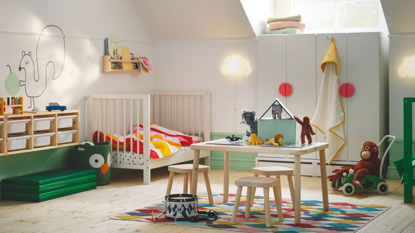 A vibrant children’s room with a white GULLIVER cot in one corner and a FLSAT children’s table and three stools on a rug.