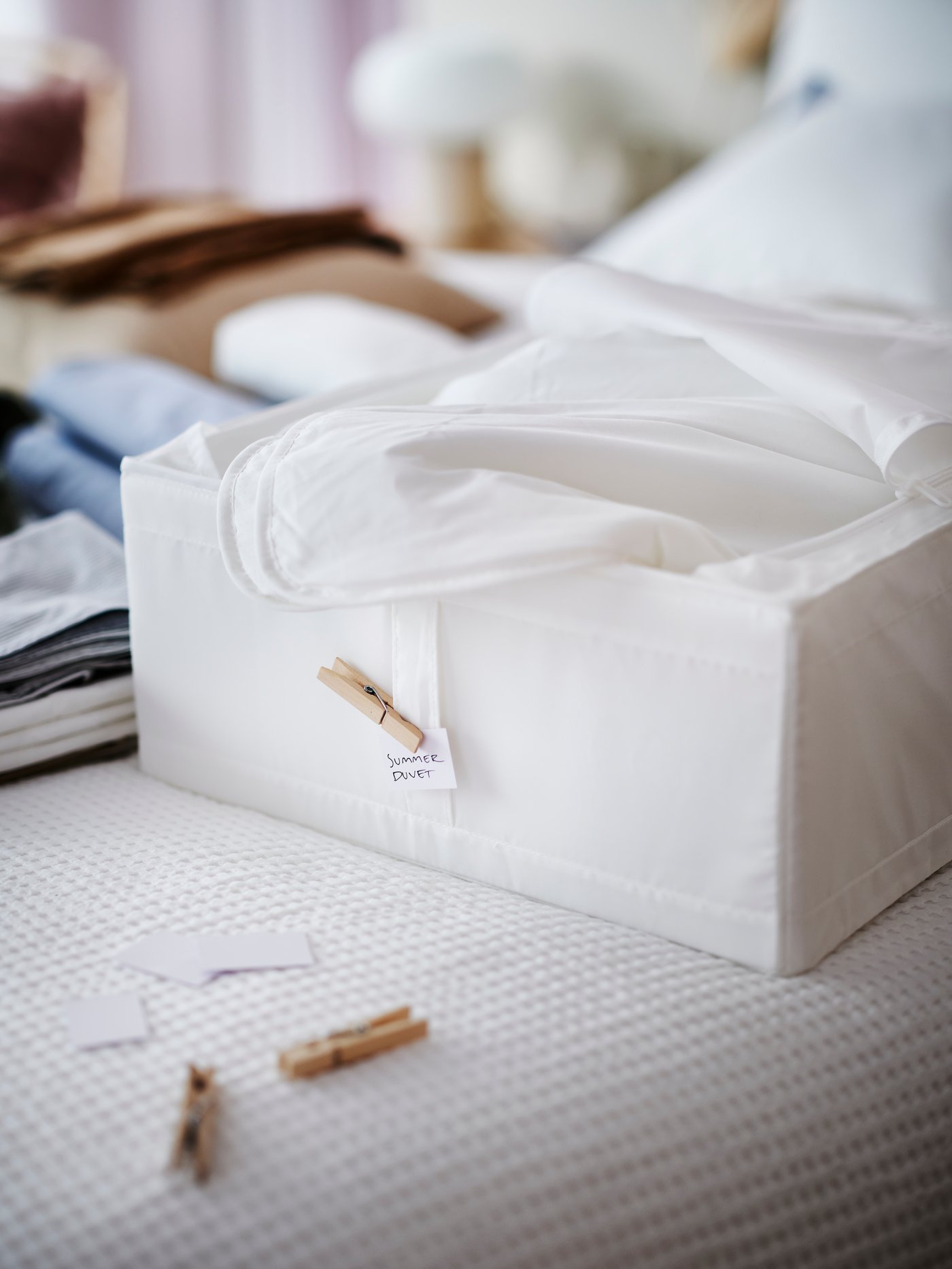 A wooden bed frame with bedding on top and a storage box with a duvet in it halfway out from under the bed.