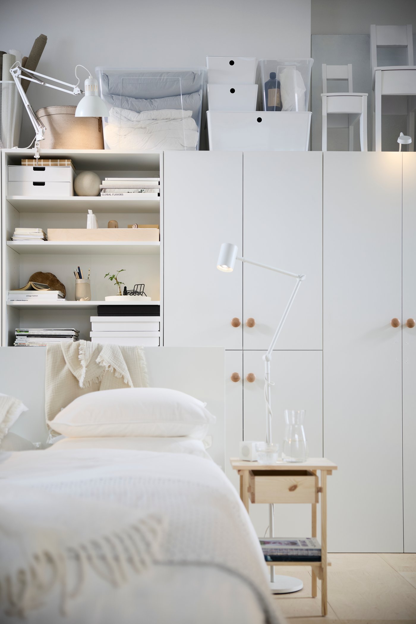Modernt minimalistiskt vitt sovrum med skandinavisk design, med en bäddad säng, vita garderober, organiserad öppen hylla och en vit justerbar golvlampa.