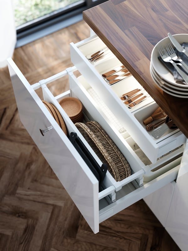 A large drawer in a cabinet with white RINGHULT kitchen kitchen cabinet doors is pulled out and there are kitchen items organised inside.