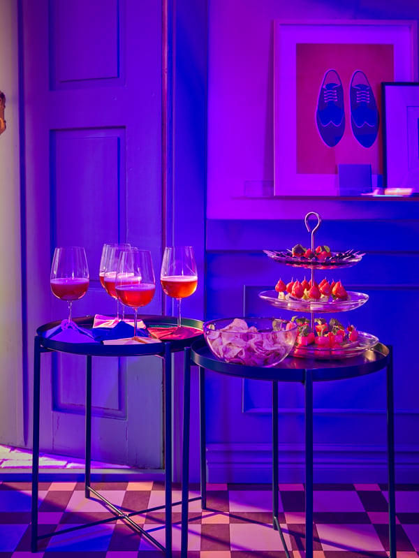 A tiled-floor hallway in purple light with welcoming bites on a KVITTERA serving stand and drinks in STORSINT wine glasses.