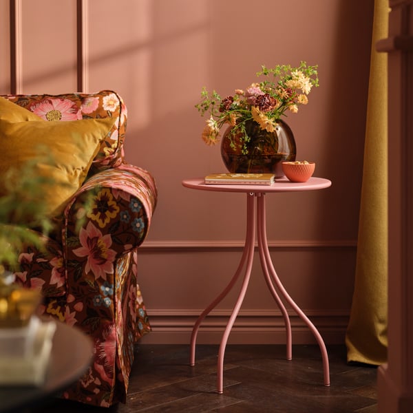 A TÅNEBRO side table in light pink stands in a pink living room next to an EKTORP sofa with a floral sofa cover.