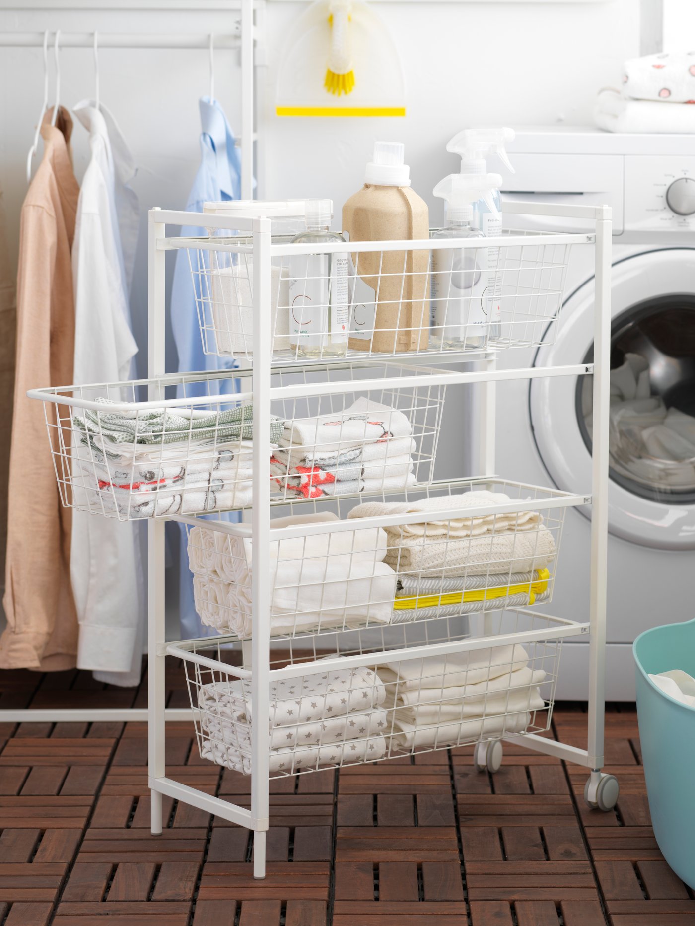 A laundry area that has a washing machine and a white JONAXEL frame with wire baskets and castors holding towels and soaps.