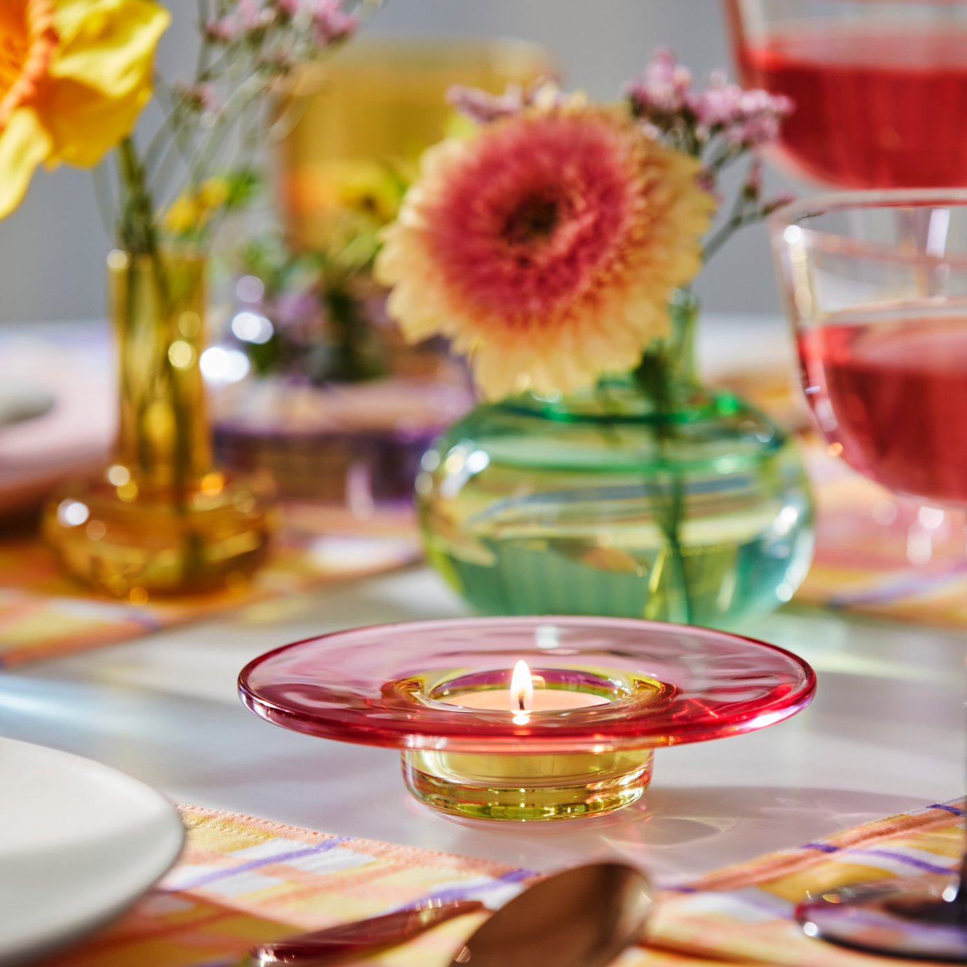 A multicoloured TJÄRLEK tealight holder with a lit tealight in the dining room.