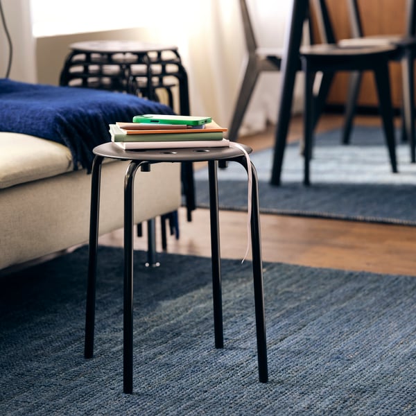 Chaises LISABO et tabouret MARIUS noir chargé de livres sur un tapis bleu.