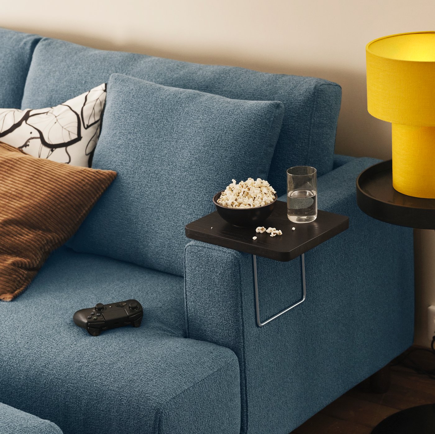 En TRANERED armlænsbakke med snacks og et glas hviler på armlænet af en mørkegrå-blå UPPÅKRA 4,5-pers. modulopbygget sofa.