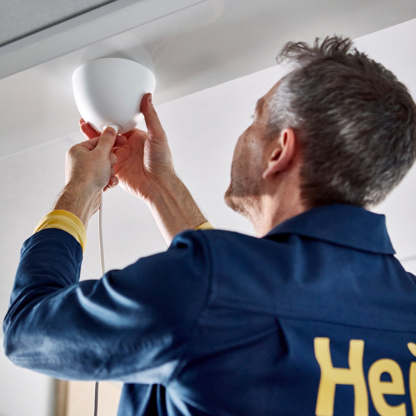 IKEA co-worker securing a lamp cord to the ceiling.