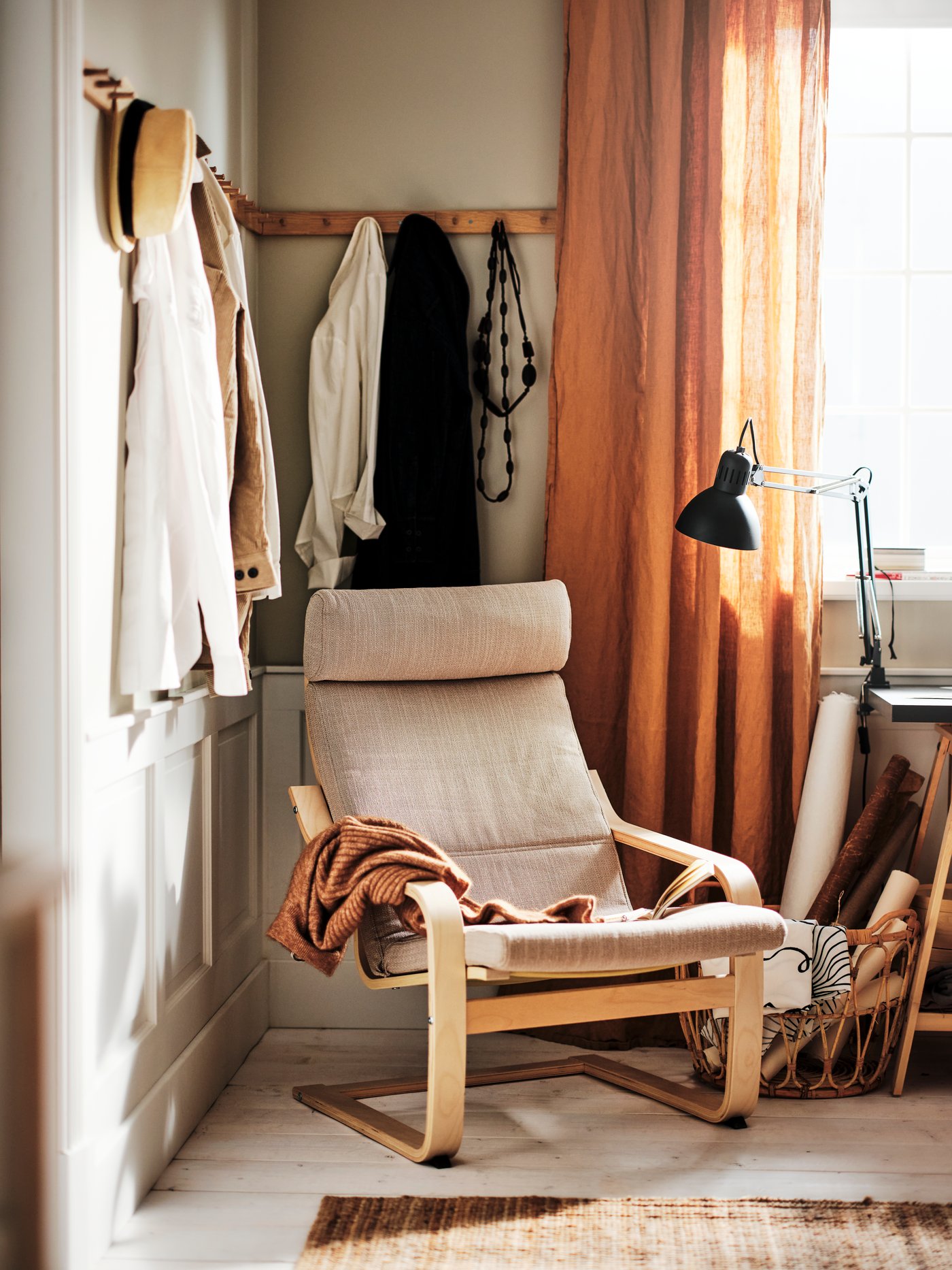 A POÄNG armchair with beige cushion placed in a corner of a room by a window.