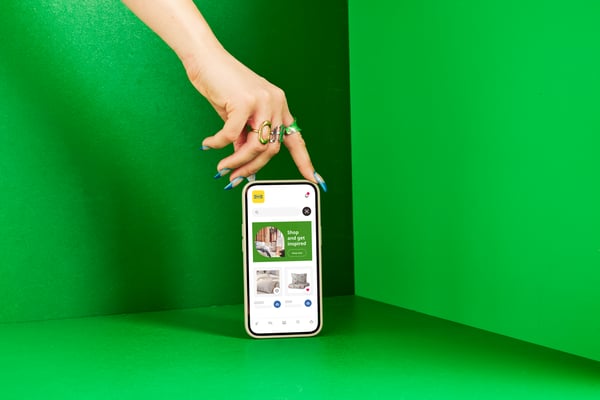 Ein Smartphone steht aufrecht vor einem grünen Hintergrund; darüber ist eine Hand zu sehen, die es elegant hält.