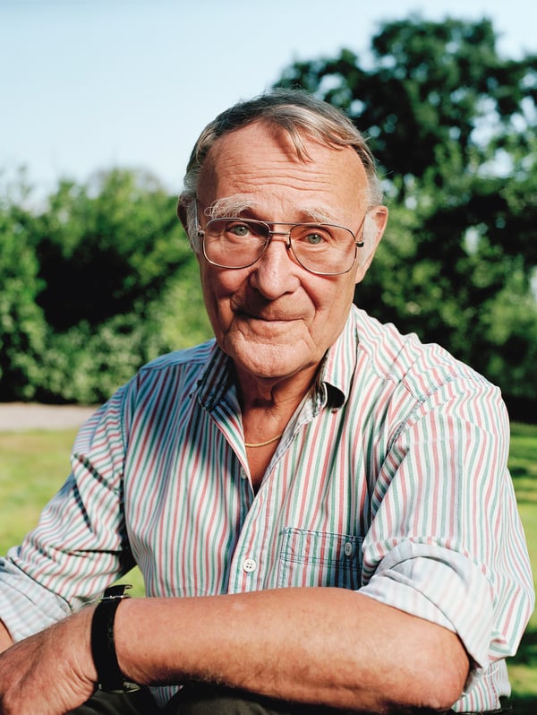 A portrait of IKEA founder Ingvar Kamprad, outdoors smiling while wearing a pink, white and green striped shirt.
