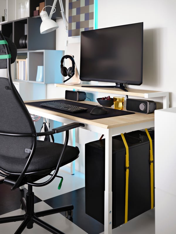 An ash effect/white UTVSNING gaming desk with shelf holds a complete PC gaming setup, including a CPU held by yellow straps.