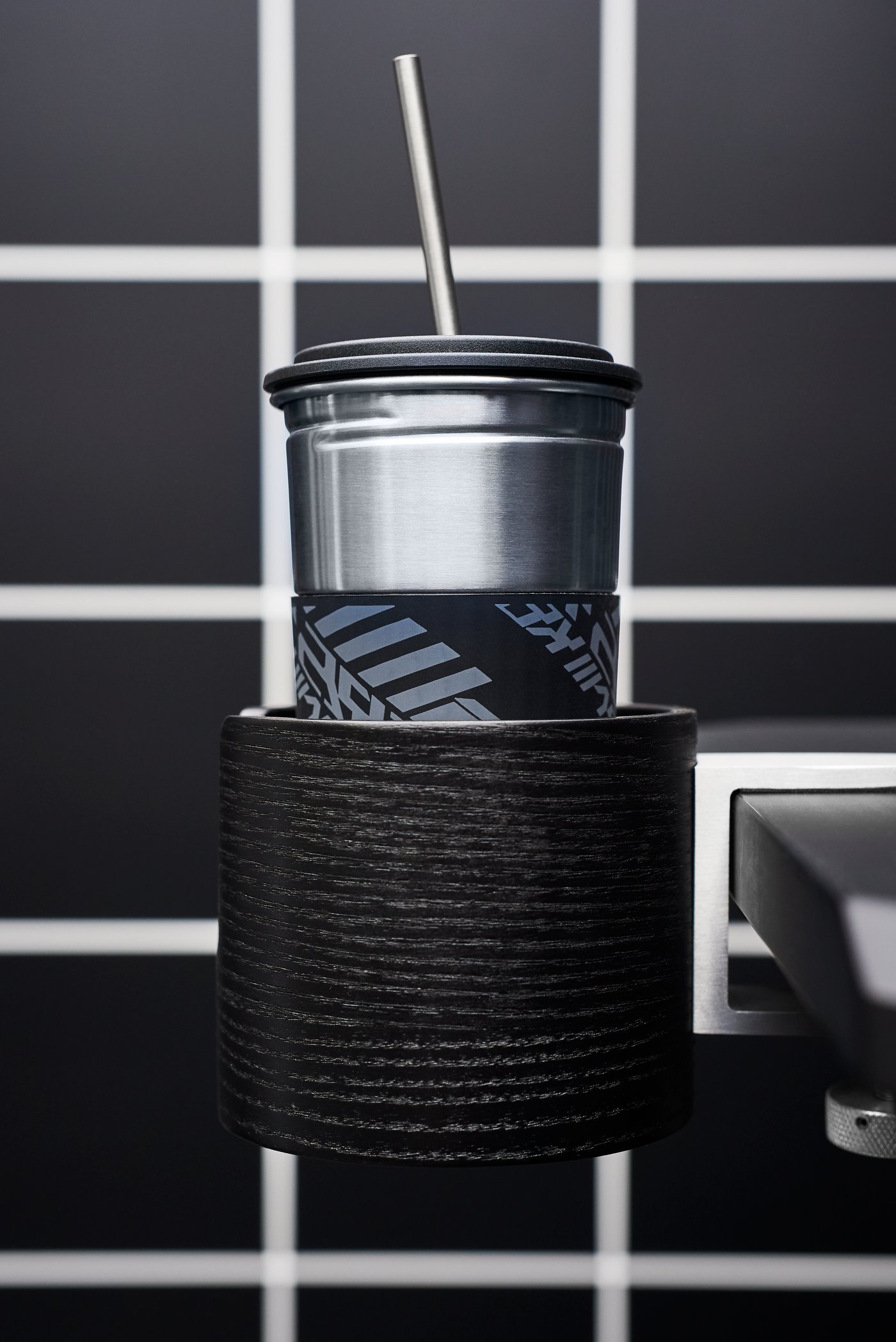 Mug with a lid and a straw holder attached to a computer gamer’s black desk with headphones in the blue background.