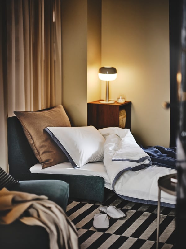 A single‑seat KIVIK sofa bed made up as a bed in the living room, placed on a black‑and‑white TÅSJÖN rug.