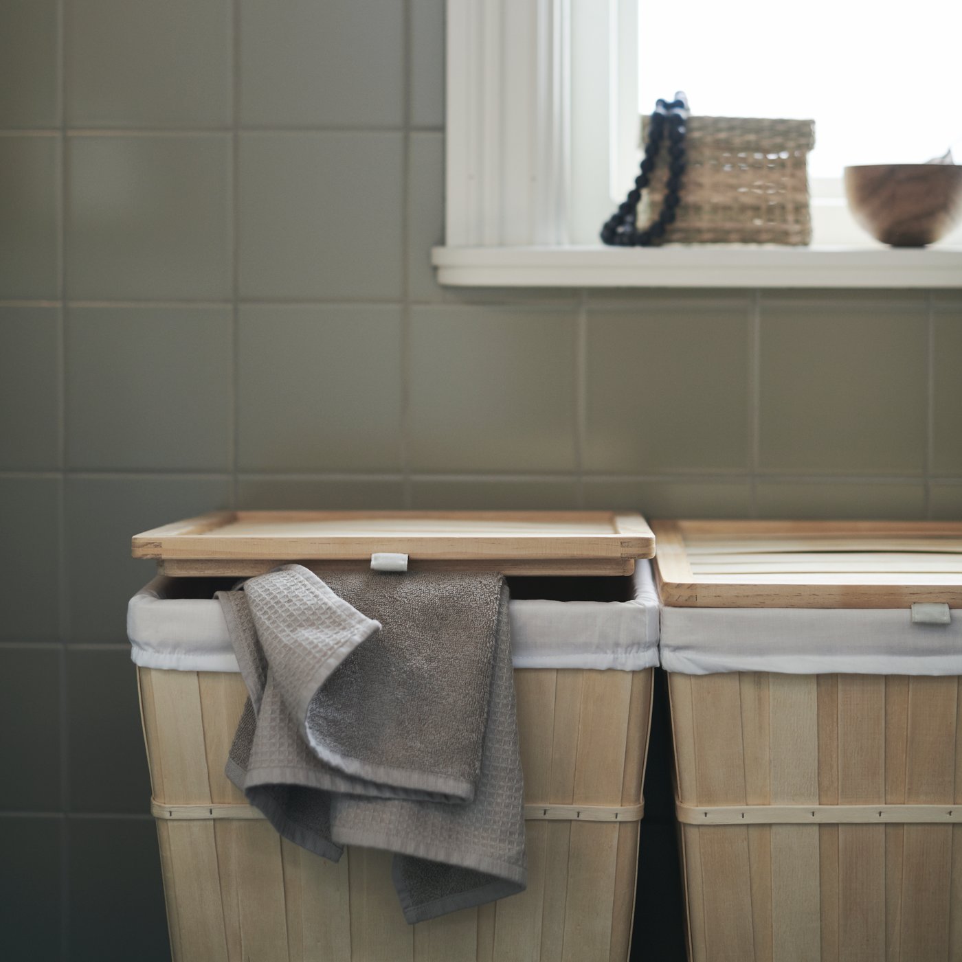 Two side-by-side BRANKIS laundry baskets in a green-tiled bathroom.