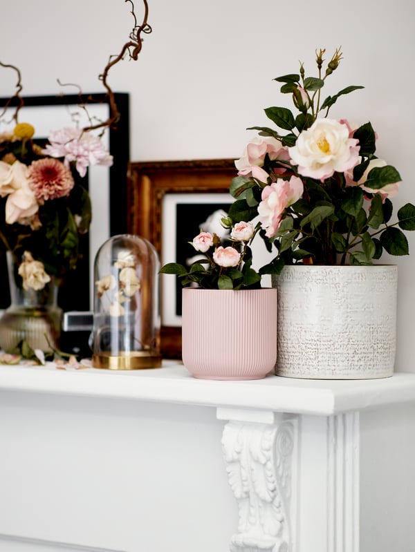 Un muele blanco con cuadros decorativos y plantas en el que destaca un macetero rosado GRADVIS con unas flores del mismo color.