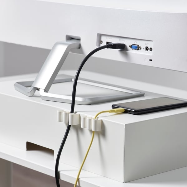 Auf der Rückseite eines Monitorständers sind weiße KALKSTUFF Kabelhalter aus Kunststoff befestigt. Sie halten ein Telefon- und ein HDMI-Kabel an Ort und Stelle.