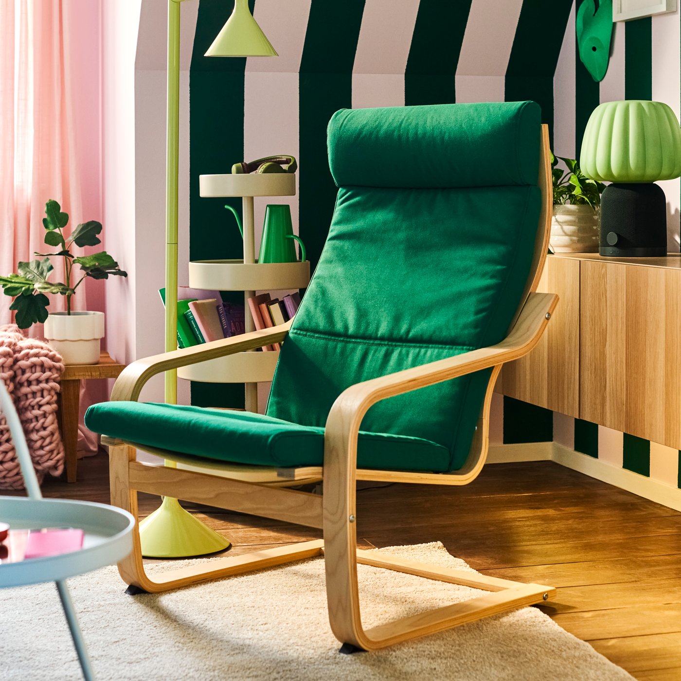 A modern living room has a bentwood frame POÄNG armchair with a deep green cushion, by a corner wall with big, green stripes.