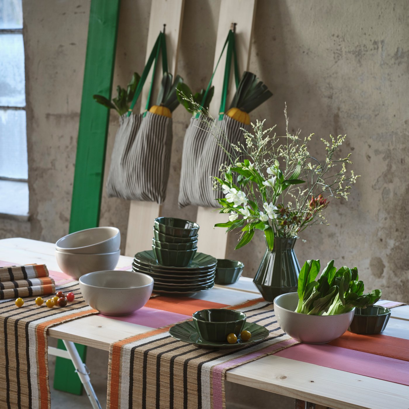 A wooden table in an industrial-style room is set with various table essentials from the MÄVINN collection.