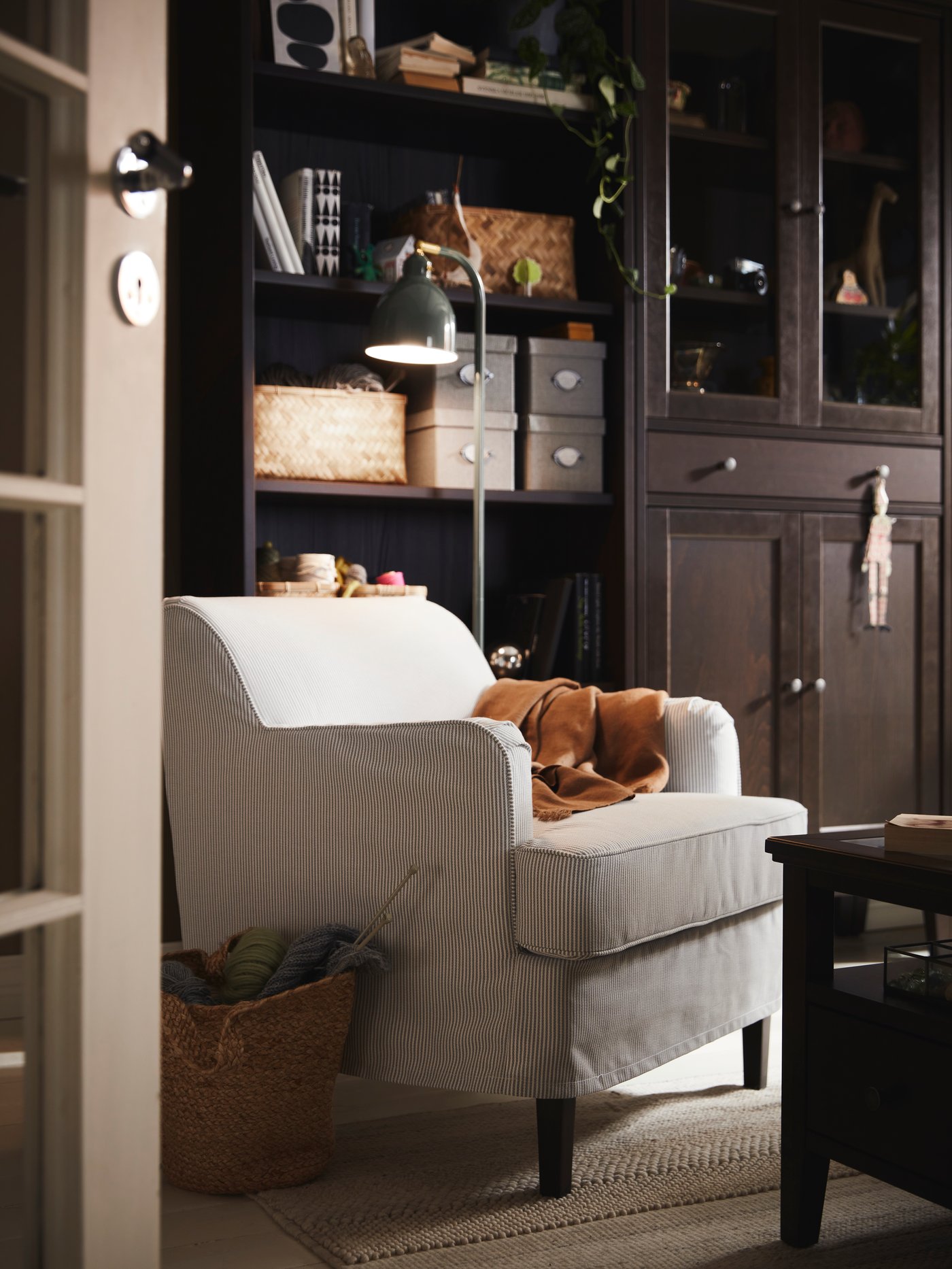 A ROCKSJÖN armchair with a light brown DYTÅG throw stands in a corner near an IDANÄS bookcase and a high cabinet.