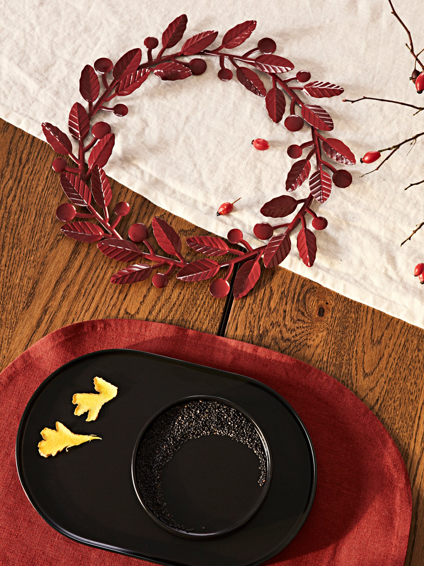 A table set with a red KRÖSAMOS place mat and a black KRÖSAMOS serving plate and serving bowl and a red KRÖSAMOS wreath.
