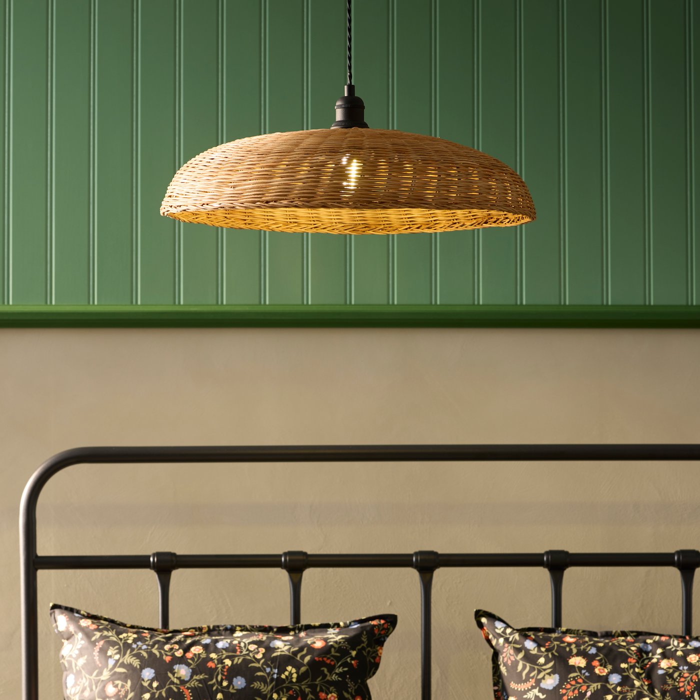 A rattan NARRKOLV pendant lamp against a green wall above floral bedding.