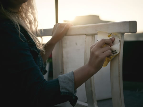 Ruke koriste žuti sunđer za čišćenje bele površine, a sunčeva svetlost prodire u pozadini. Slika sugeriše temu čistoće, nege i održivosti. Reč „huit” se vidi na slici, verovatno kao deo većeg, nevidljivog konteksta.