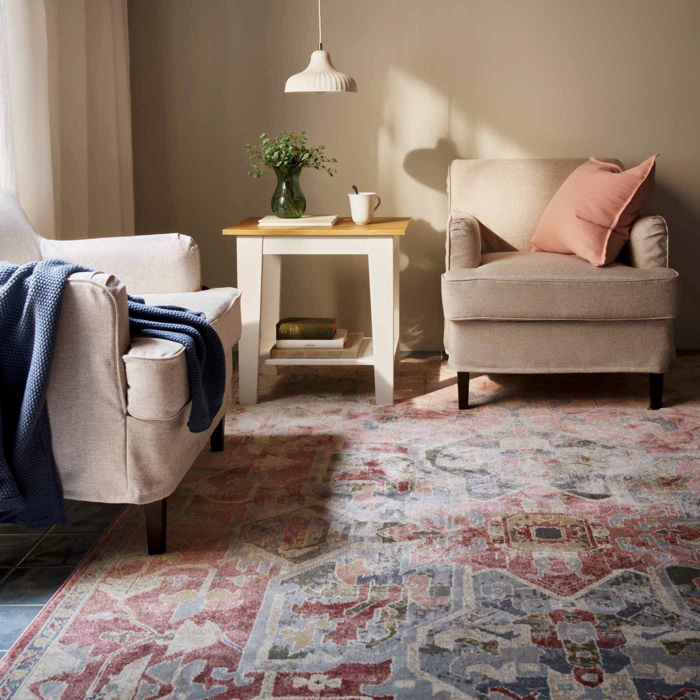 A living room with a pink-beige, ornamental-pattern JÄRNVÄG low-pile rug placed beneath two chairs and a table.