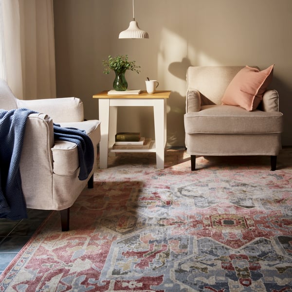 A living room with a pink-beige, ornamental-pattern JÄRNVÄG low-pile rug placed beneath two chairs and a table.