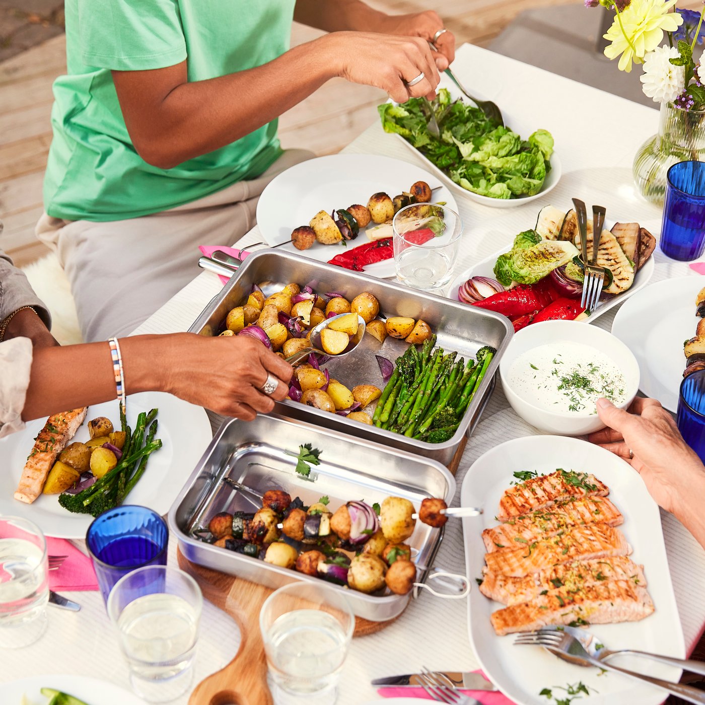 Groupe de personnes se servant du filet de saumon SJÖRAPPORT, des pommes de terre rôties et des légumes dans des plats de service IKEA 365+.