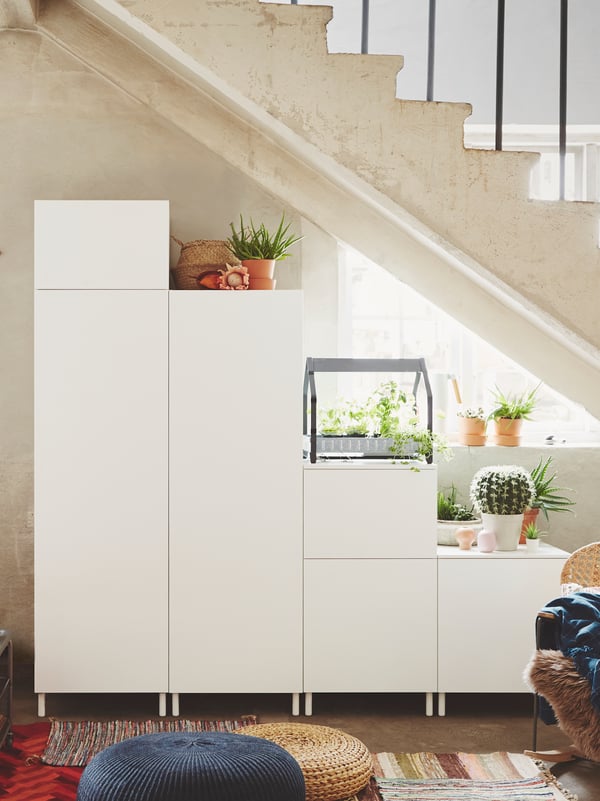 Ein moderner weisser Schrank mit vielen Fächern, dekoriert mit Pflanzen, in einer stylischen Einrichtung.