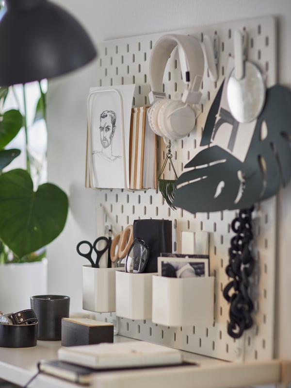 A wall in a workspace which has five SKÅDIS pegboards placed next to each other filled with frames, drawings and artwork.