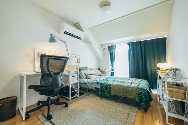 手前にグレーラグが敷かれた部屋に、デスクとベッドが置かれている様子