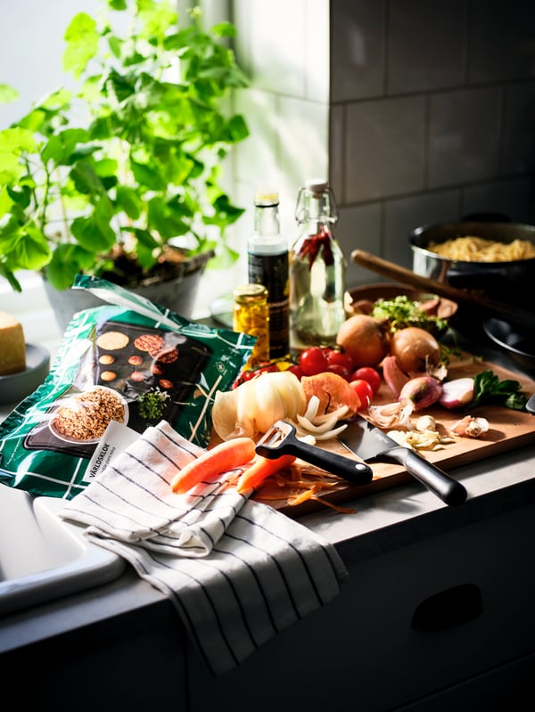 A worktop filled with ingredients in the middle of cooking prep, a RINNIG tea towel, and a bag of VÄRLDSKLOK plant mince.