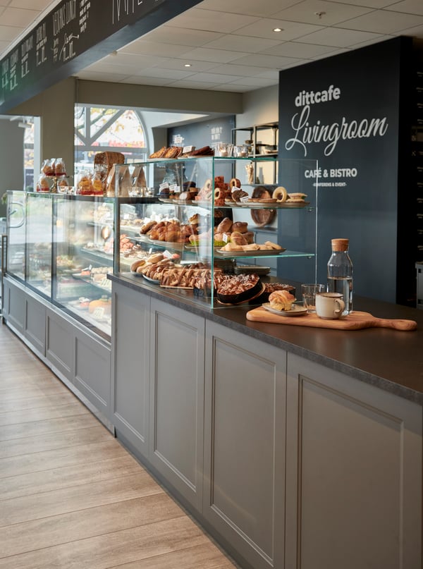 En lång grå kassadisk i ett cafe där man ser glasskåp och kyldiskar med bakverk. 
