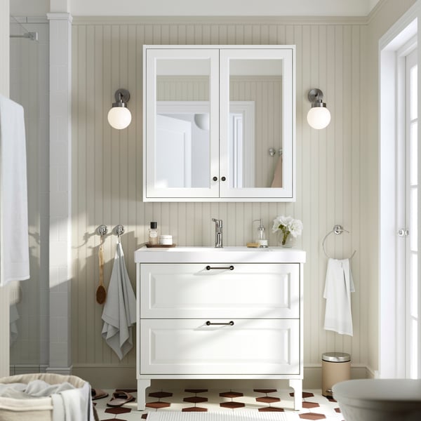 A bright bathroom with beige walls has a white TÄNNFORSEN vanity with two drawers, a white mirror cabinet and two lamps.
