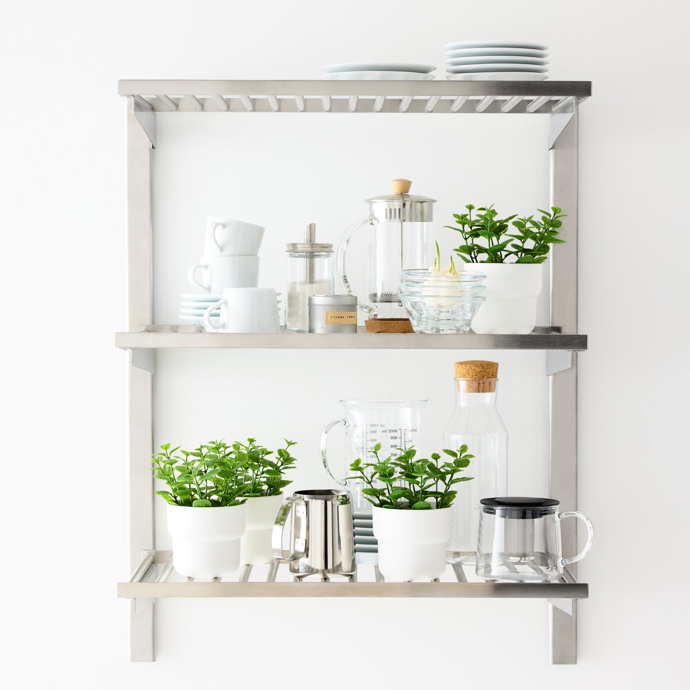 Four green FEJKA artificial plants on a wall-mounted kitchen shelf, next to kitchenware in white, glass and stainless steel.