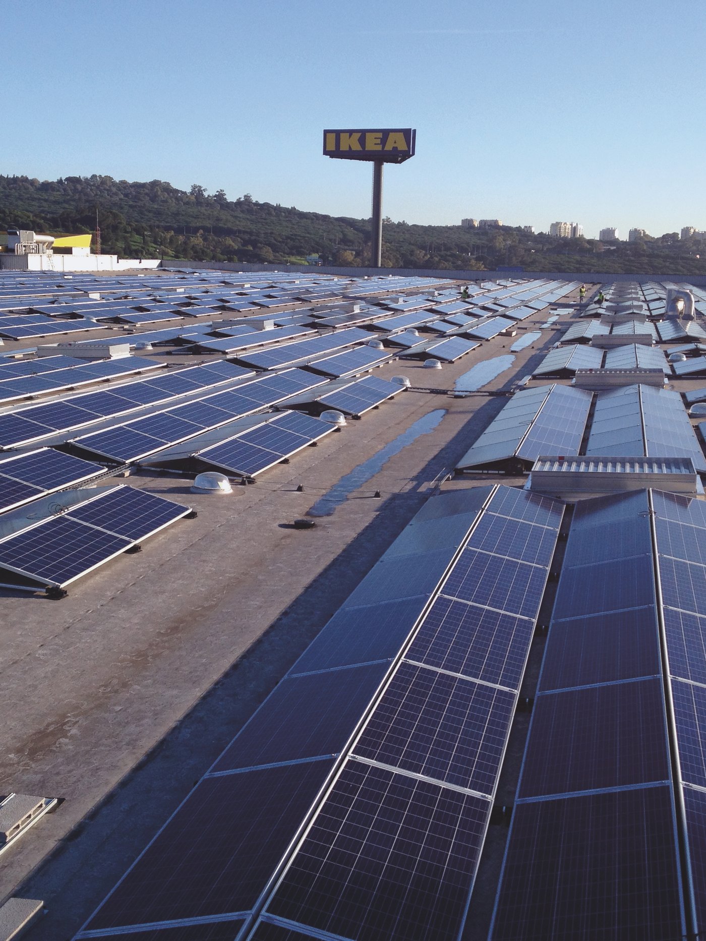 Niz stotina solarnih panela na krovu IKEA objekta. U pozadini je veliki trostrani IKEA znak.