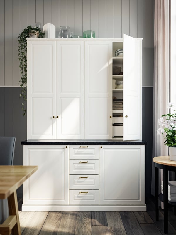 A traditional-looking closed storage unit with white fronts and drawers and brass-coloured handles and knobs.