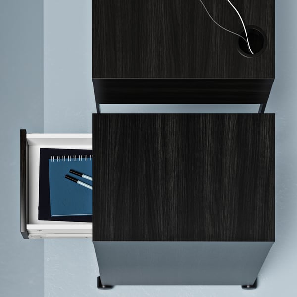 A MICKE drawer unit, its drawer pulled out to reveal notebooks and pens, placed next to a MICKE desk.