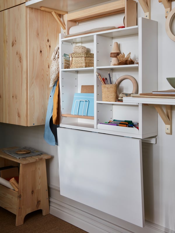 A NORBERG wall-mounted drop-leaf table and storage holding pens, books and small storage. The table’s leaf is folded down.
