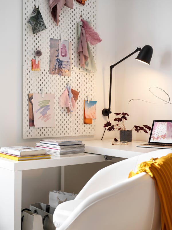 Espacio de estudio con escritorio de color blanco, con un organizador de pared  una lampara de escritorio de color negro.