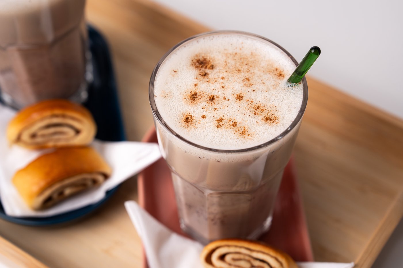 Ein Haferlatte in einem Glas, welches mit Zimtschnecken auf einem Holztablett präsentiert wird.