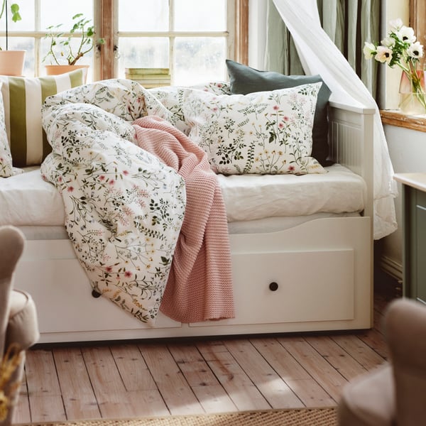 En lantlig sovrumshörna med bäddsoffa och blommiga textilier.