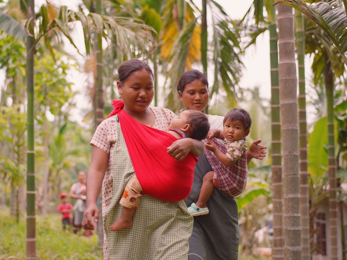 A family in the nature walking forward with two childrens in their arms. 