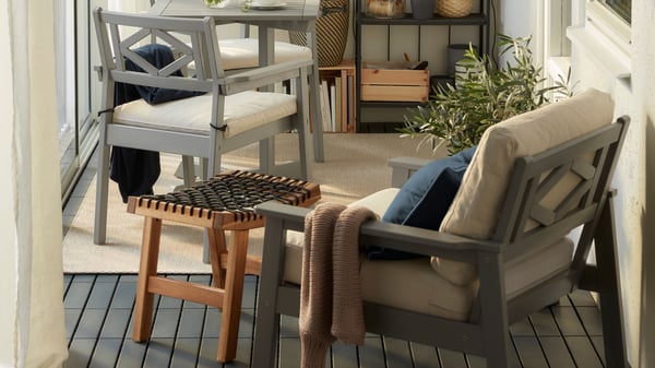 A corner shot of a BONDHOLMEN chair with a beige cushion. The room has various outdoor furniture all sitting on gray RUNNEN flooring.