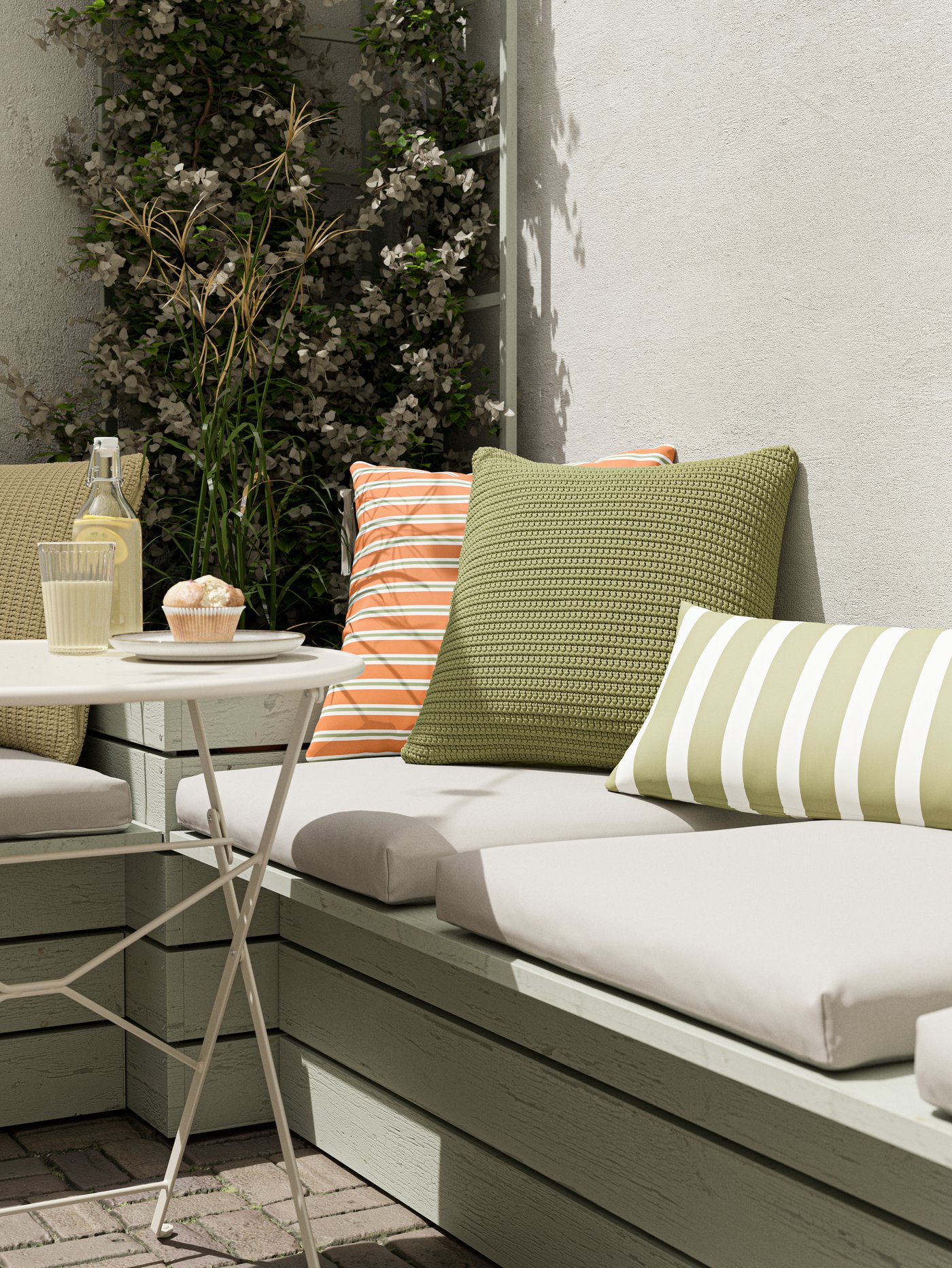 A sitting ledge with beige seat cushions, green and orange cushions, and a table with a cupcake and lemonade on it.