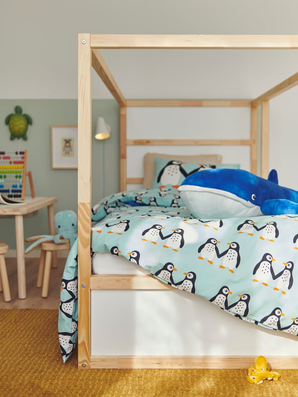 A BLÅVINGAD soft toy blue whale lies on a duvet with a BLÅVINGAD duvet cover at the foot of a KURA reversible bed.
