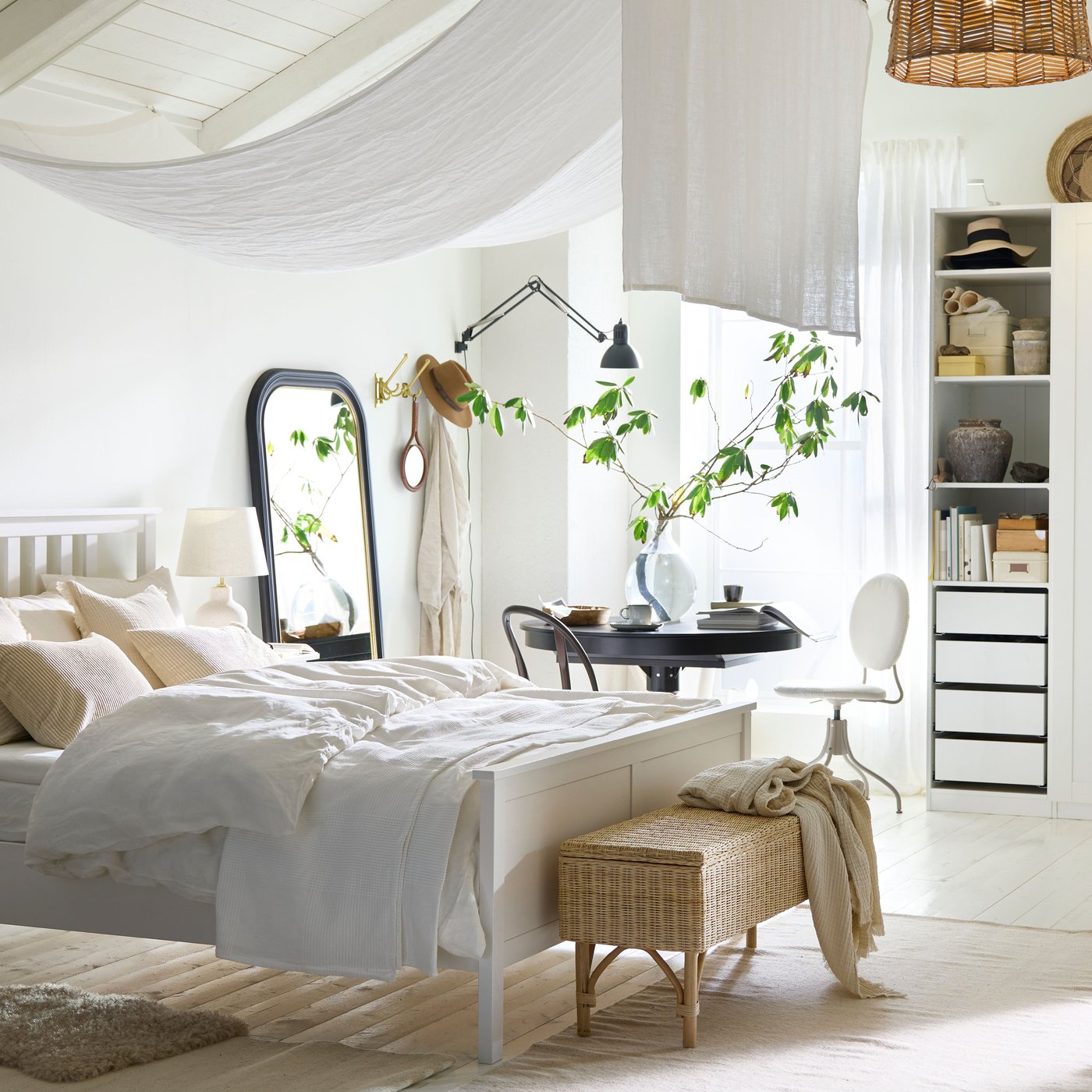 A white HEMNES double bed in a bright airy white bedroom with a black INGATORP extendable table by a window behind it.
