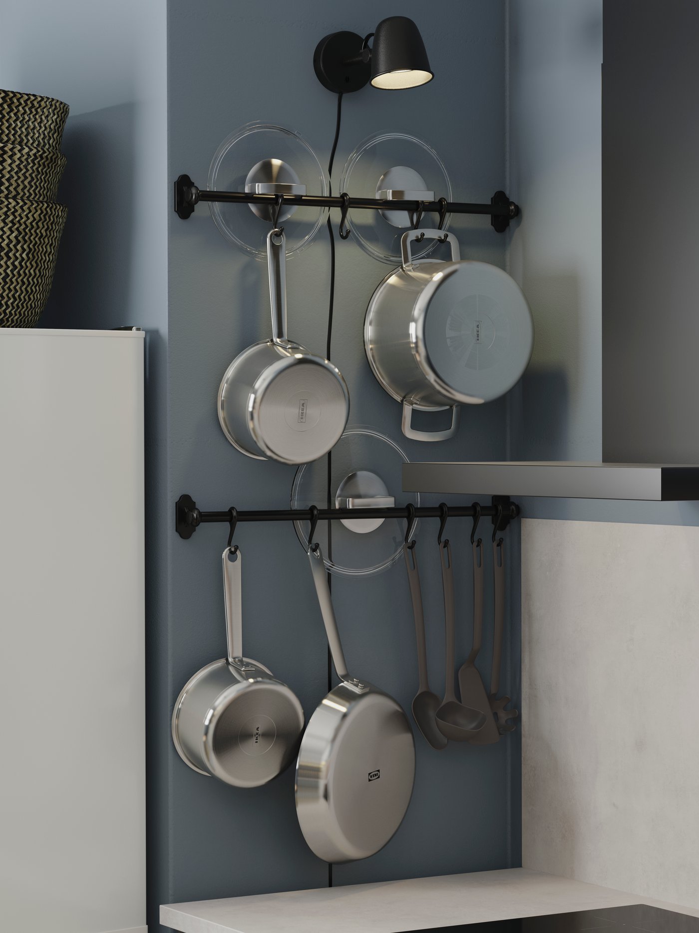 Two black rails with hooks where saucepans, pots, frying pans and lids are stored. A black, lit wall lamp is above.