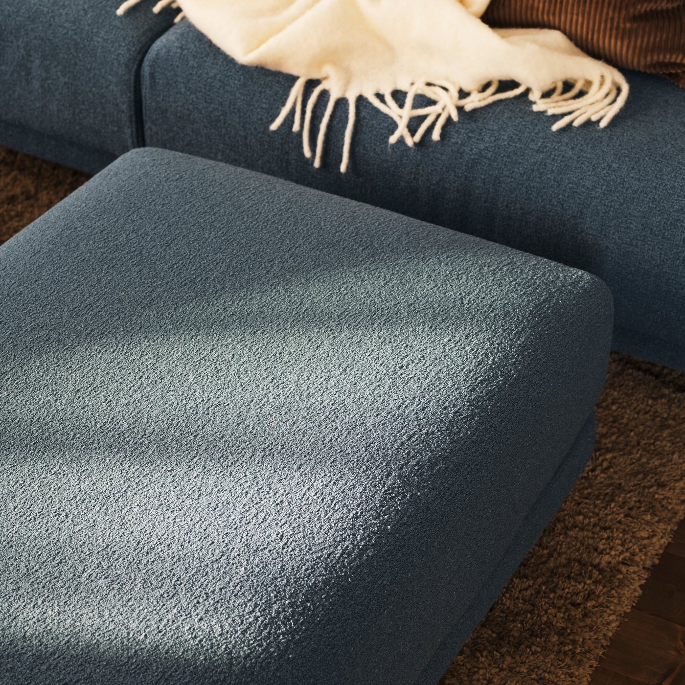 One of the cushions of a dark grey-blue UPPÅKRA 4.5-seat modular sofa lying on the floor beside the sofa.